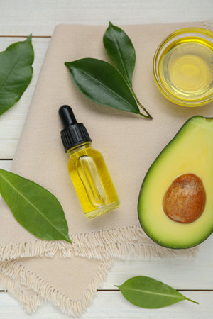 Essential oil, ripe fresh avocado and leaves on white wooden table, flat layの写真素材