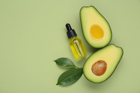 Essential oil, fresh cut avocados and leaves on light green background, flat lay. Space for textの写真素材