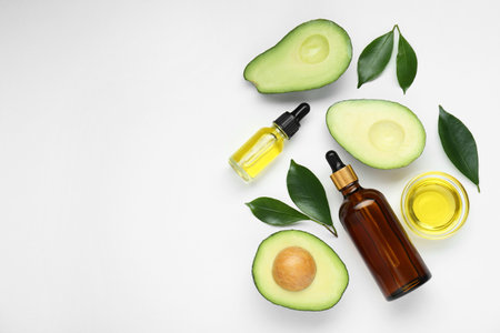 Essential oil, fresh cut avocados and leaves on white background, flat lay. Space for textの写真素材