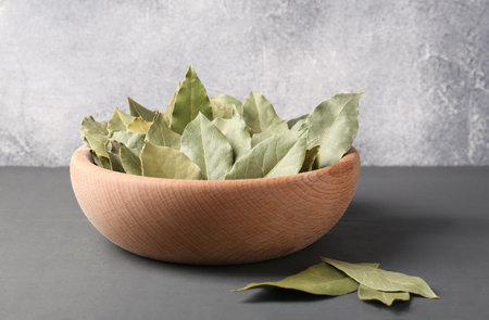 Aromatic bay leaves in wooden bowl on gray table
