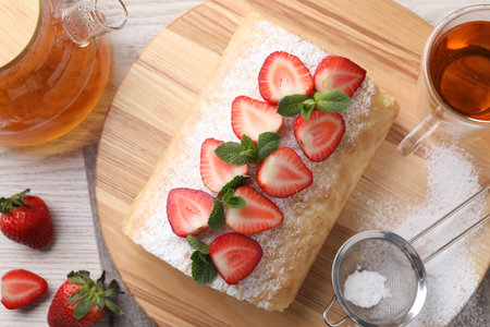 Delicious cake roll with strawberries and tea on wooden board, flat layの写真素材