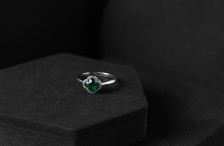 Beautiful ring with green gemstone on black podium, space for text. Luxury jewelry