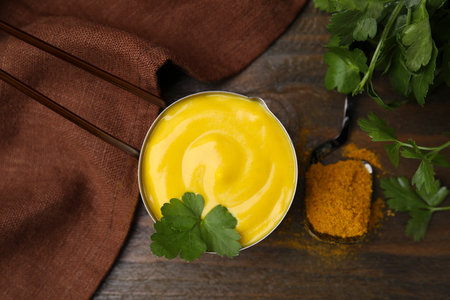 Saucepan with tasty curry sauce, powder and parsley on wooden table, flat layの写真素材