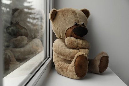 Cute lonely teddy bear on windowsill indoors. Space for textの写真素材