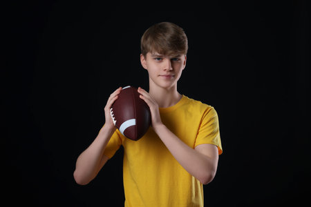 Teenage boy with american football ball on black backgroundの写真素材
