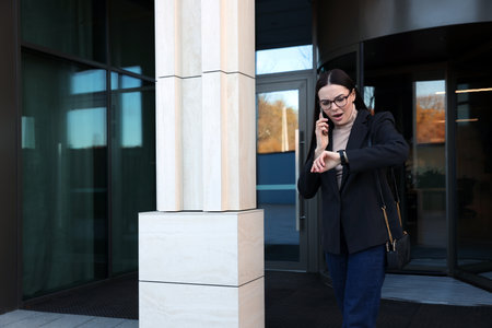 Emotional woman checking time while talking on smartphone outdoors. Being late conceptの写真素材