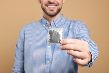 Happy man holding condom on beige background, closeupの写真素材