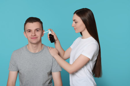 Woman spraying medication into man's ear on light blue backgroundの写真素材