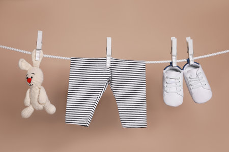Cute small baby shoes, pants and toy hanging on washing line against brown backgroundの写真素材