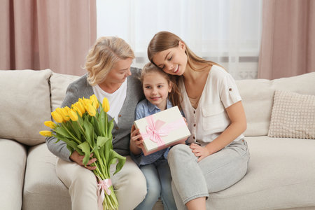 Little girl congratulating her mom and granny with flowers and gift at home. Happy Mother's Day