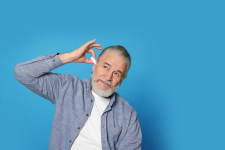 Senior man using ear drops on light blue background, space for textの写真素材