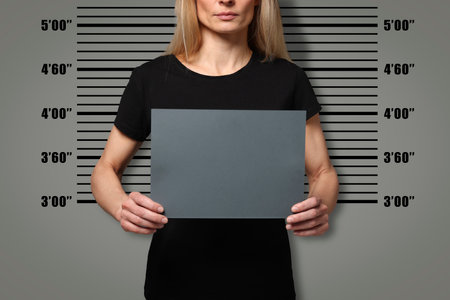 Criminal mugshot. Arrested woman with blank card against height chart, closeupの写真素材