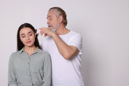 Senior man spraying medication into woman's ear on white background, space for textの写真素材