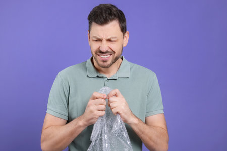 Angry man popping bubble plastic wrap on purple background. Stress reliefの写真素材