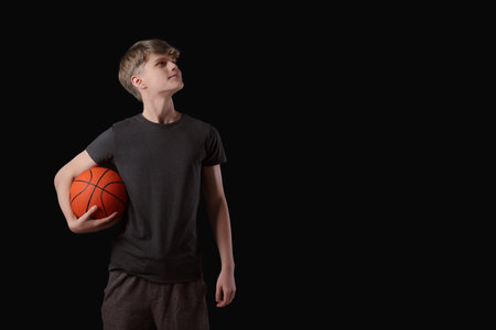 Teenage boy with basketball ball on black background. Space for textの写真素材