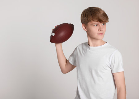 Teenage boy with american football ball on light gray background. Space for textの写真素材