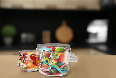 Glass jars with tasty gummy candies on light brown table in kitchen. Space for textの写真素材