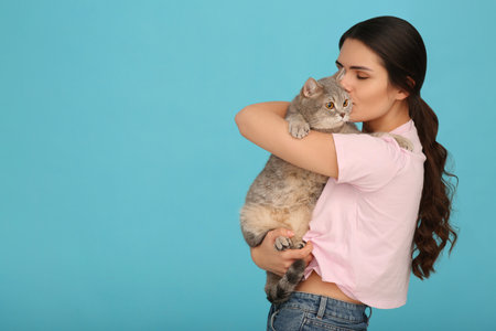 Young woman kissing her adorable cat on light blue background, space for textの写真素材