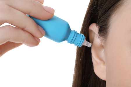 Woman using ear drops on white background, closeup