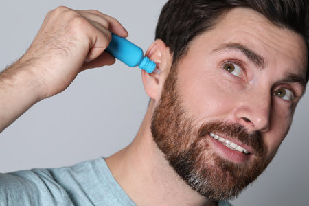 Man using ear drops on gray background, closeup