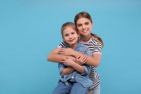 Young woman hugging her little daughter on light blue background, space for text. Happy Mother's Dayの写真素材