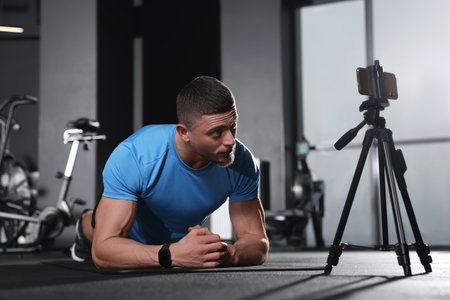 Trainer streaming online workout with phone at gym