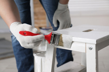 Man using brush to paint bekvam with white dye indoors, closeup