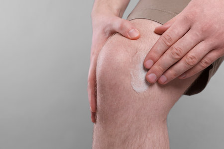 Man applying ointment onto his knee on light gray background, closeup. Space for textの写真素材