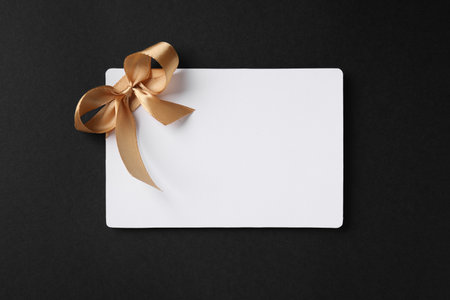 Blank gift card with golden bow on black background, top view. Space for textの写真素材