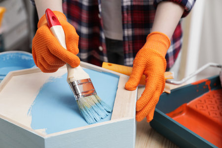 Woman painting honeycomb shaped shelf with brush at wooden table, closeupの写真素材