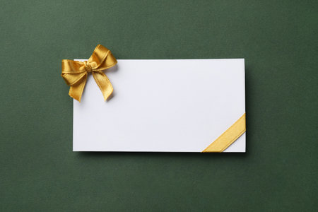 Blank gift card with golden bow on dark green background, top viewの写真素材