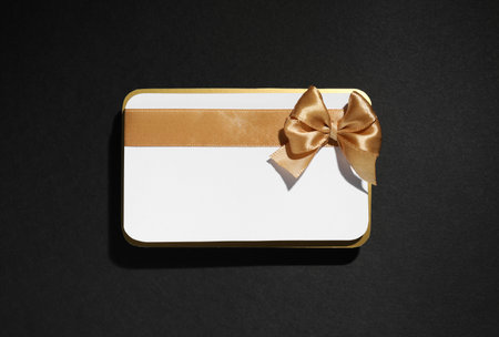 Blank gift card with golden bow on black background, top viewの写真素材