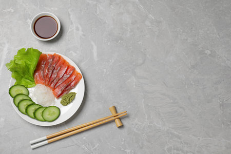 Sashimi set (salmon slices) with cucumber, greens, wasabi and funchosa served with soy sauce on light gray table, flat lay. Space for textの写真素材