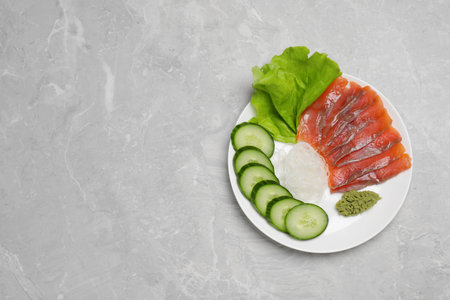 Sashimi set (salmon slices) with cucumber, greens, wasabi and funchosa on light gray table, top view. Space for textの写真素材
