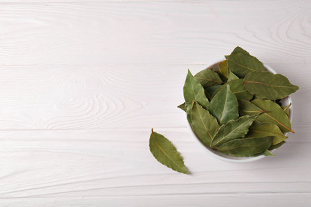 Dry bay leaves in bowl on white wooden table, flat lay. Space for textの写真素材