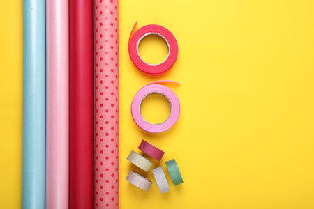 Rolls of colorful wrapping papers and ribbons on yellow background, flat lay. Space for textの写真素材