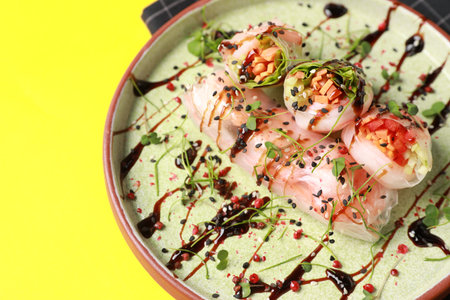 Plate of delicious spring rolls with sauce and microgreens on yellow background, closeup