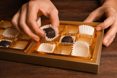 Woman taking chocolate candy out from box at wooden table, closeupの写真素材