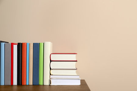 Many different hardcover books on wooden table near beige wall. Space for textの写真素材