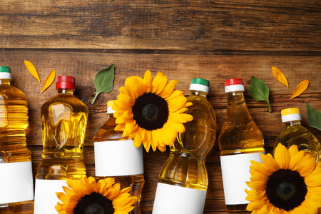 Bottles of sunflower cooking oil and beautiful flowers on wooden table, flat lay. Space for textの写真素材