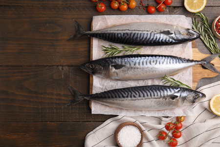 Raw mackerel, tomatoes and rosemary on wooden table, flat lay. Space for textの写真素材