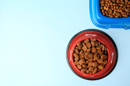 Dry pet food in feeding bowls on light blue background, flat lay. Space for textの写真素材