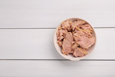 Bowl with canned tuna on white wooden table, top view. Space for textの写真素材