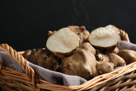 Wicker basket with many Jerusalem artichokes against dark background, closeupの写真素材