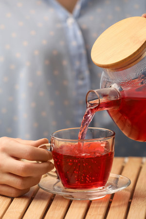 Woman pouring delicious hibiscus tea into cup at wooden table, closeupの写真素材
