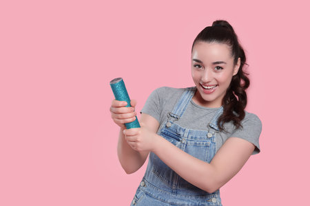 Young woman blowing up party popper on pink background, space for text