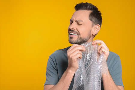 Man popping   wrap on yellow background, space for text. Stress relief