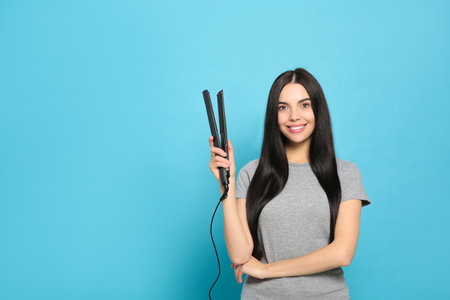 Beautiful happy woman with hair iron on light blue background. Space for textの写真素材