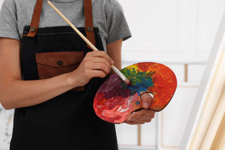 Woman mixing paints on palette with brush near easel in studio, closeupの写真素材
