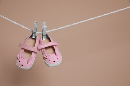 Cute small baby shoes hanging on washing line against brown background, space for textの写真素材